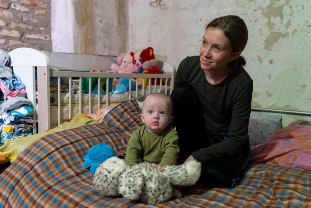 KHARKIV, UKRAINE – OCTOBER 6: Olga and her son Yevhen with soft toy sit on the bed in the improvised child room at the factory shelter on October 6, 2022 in Kharkiv, Ukraine. In Kharkiv, almost two dozen people from the suburbs have been living in the bunker of the plant for more than seven months. Their villages were de-occupied, but the people have nowhere to return. Among them is Olga and her seven-month-old son, whom she gave birth to during the war. Woman was offered to move to a sanatorium with her child, but she refused, because her husband works at the plant, and the shelter is considered safe. (Photo by Oleksandra Novosel/Suspilne Ukraine/JSC 