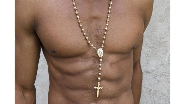 Gold cross hands from an elongated rosary chain against a background of well-defined brown abs