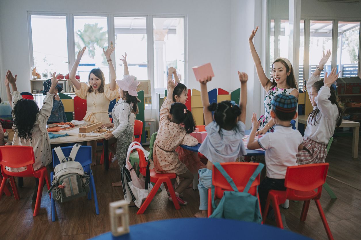 Asian Montessori preschool student raised hands in the class answering question