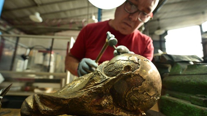 Mengintip Pembuatan Trofi Piala Dunia 2022 di Milan A worker applies manual chiselling and hammering to refine intricate details on a raw brass trophy, replica of the FIFA football World Cup Trophy, at the Italian trophy and medal manufacturer GDE Bertoni on October 12, 2022 in Paderno Dugnano, north of Milan. - While the original 18 carat gold trophy made by Italian artist Silvio Gazzaniga belongs to FIFA and is rarely exhibited, the GDE Bertoni factory is still tasked with producing brass gold-plated replicas of the trophy every four years for the winning team. (Photo by MIGUEL MEDINA / AFP) (Photo by MIGUEL MEDINA/AFP via Getty Images)