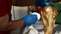 Seorang pekerja membersihkan dengan kain replika Trofi Piala Dunia sepak bola FIFA. Trofi tersebut memiliki desain unik dengan warna emas dan memperlihatkan dua orang mengangkat bola dunia.