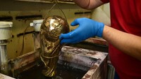 Seorang pekerja mencelupkan replika kuningan mentah dari Trofi Piala Dunia sepak bola FIFA ke dalam bak degreasing. Selama bertahun-tahun, GDE Bertoni dipercaya untuk memproduksi trofi Piala Dunia.