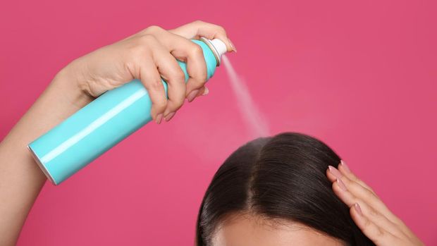 Young woman applying dry shampoo against pink background, closeup