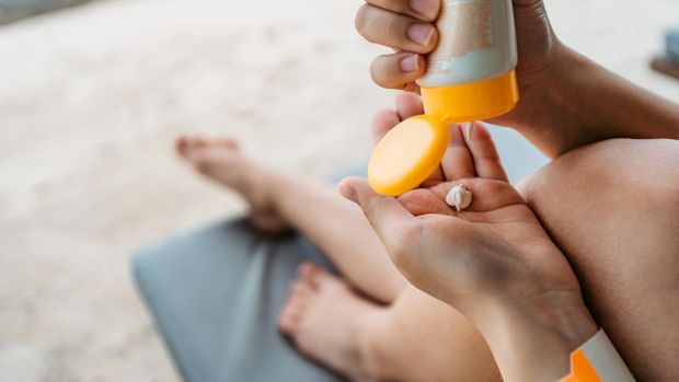 Woman hand apply sunscreen on the beach, close up.