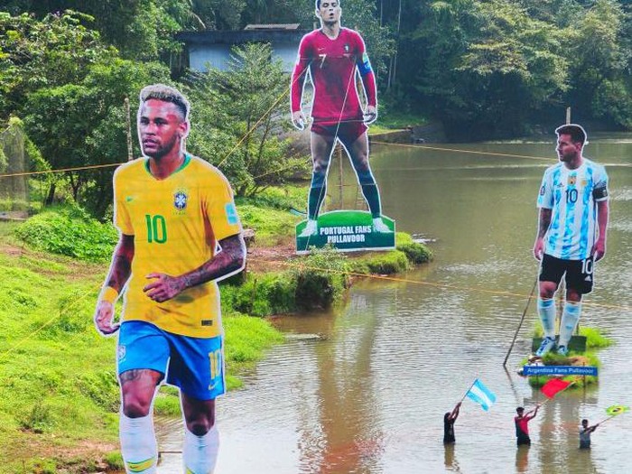 Fans wave flags next to the giant cutouts of players from Brazil's Neymar (L), Portuguese Cristiano Ronaldo (C) and Argentine Lionel Messi, erected by football fans in river Cherupuzha at Kozhikode in India's Kerala state on November 7, 2022, ahead of the Qatar 2022 FIFA World Cup football tournament. (Photo by AFP) (Photo by -/AFP via Getty Images)
