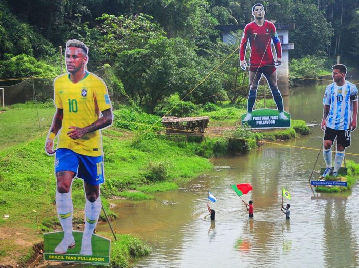 Fans wave flags next to the giant cutouts of players from Brazil's Neymar (L), Portuguese Cristiano Ronaldo (C) and Argentine Lionel Messi, erected by football fans in river Cherupuzha at Kozhikode in India's Kerala state on November 7, 2022, ahead of the Qatar 2022 FIFA World Cup football tournament. (Photo by AFP) (Photo by -/AFP via Getty Images)