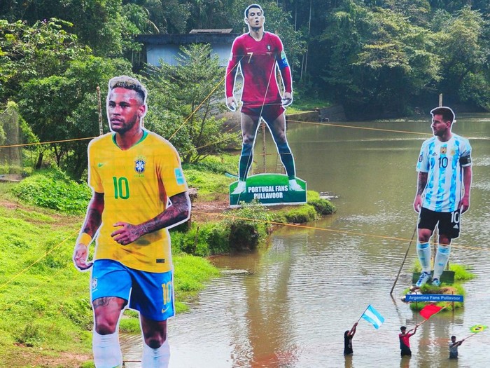 Fans wave flags next to the giant cutouts of players from Brazil's Neymar (L), Portuguese Cristiano Ronaldo (C) and Argentine Lionel Messi, erected by football fans in river Cherupuzha at Kozhikode in India's Kerala state on November 7, 2022, ahead of the Qatar 2022 FIFA World Cup football tournament. (Photo by AFP) (Photo by -/AFP via Getty Images)