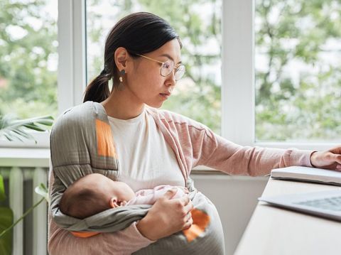 Asian young woman holding her baby on hands while making notes at the table she working at home