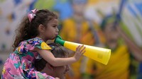 Seorang anak perempuan digendong ayahnya, meniup vuvuzela di depan pesawat bekas yang dihiasi dengan tema tim sepak bola nasional Brasil di sebuah pusat perbelanjaan di Contagem, negara bagian Minas Gerais, Brasil, Sabtu (19/11/2022). (Douglas magno/Getty Images)