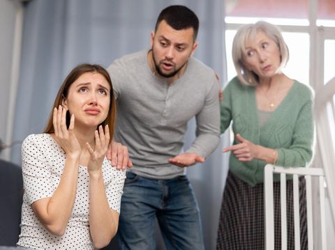 Offended woman sitting on sofa in apartment. Her husband and mother-in-law quarreling with her.