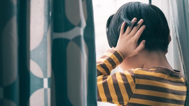Little Asian boy wear long sleeve stripe shirt stand by window, hand cover ears, crying and screaming. Feeling frustration, anxiety, fear, stressed. Domestic violence, Autism, Bipolar disorder and mental illness concept.