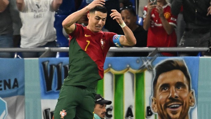 Cristiano Ronaldo TOPSHOT - Portugal's forward #07 Cristiano Ronaldo celebrates after scoring his team's first goal from the penalty spot as a banner depicting Argentine forward Lionel Messi is seen at the back during the Qatar 2022 World Cup Group H football match between Portugal and Ghana at Stadium 974 in Doha on November 24, 2022. (Photo by MANAN VATSYAYANA / AFP) (Photo by MANAN VATSYAYANA/AFP via Getty Images)