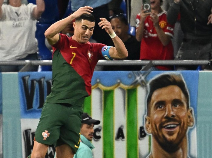 TOPSHOT - Portugals forward #07 Cristiano Ronaldo celebrates after scoring his teams first goal from the penalty spot as a banner depicting Argentine forward Lionel Messi is seen at the back during the Qatar 2022 World Cup Group H football match between Portugal and Ghana at Stadium 974 in Doha on November 24, 2022. (Photo by MANAN VATSYAYANA / AFP) (Photo by MANAN VATSYAYANA/AFP via Getty Images)