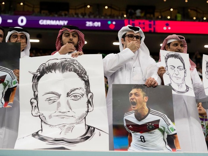 AL KHOR, QATAR - NOVEMBER 27: People in the stands hold portraits of German football player Mesut Özil in a protest against Uyghur discrimination in China during the FIFA World Cup Qatar 2022 Group E match between Spain and Germany at Al Bayt Stadium on November 27, 2022 in Al Khor, Qatar. (Photo by Sebastian Frej/MB Media/Getty Images)