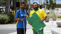 Dengan menggunakan menggunakan papan berbentuk lapangan, Helio, membantu Carlos ikut menyaksikan jalannya pertandingan piala dunia.  
