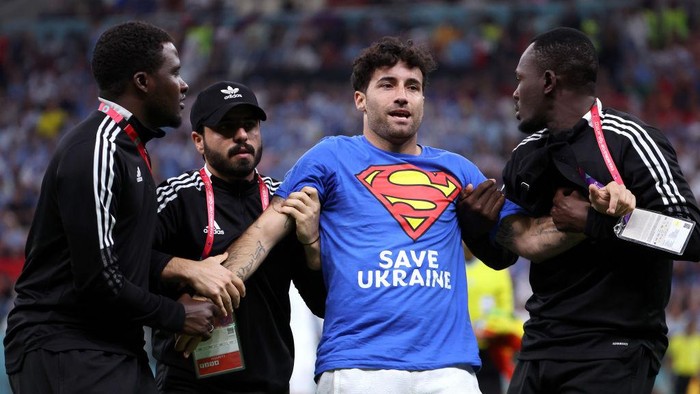 LUSAIL CITY, QATAR - NOVEMBER 28: A pitch invader - Mario Ferri - is held by security after running onto the pitch wearing a t-shirt with a message saying: 'Respect for Iranian Woman' on the back, 'Save Ukraine' in the front and holding a rainbow flag during the FIFA World Cup Qatar 2022 Group H match between Portugal and Uruguay at Lusail Stadium on November 28, 2022 in Lusail City, Qatar. (Photo by Jean Catuffe/Getty Images)