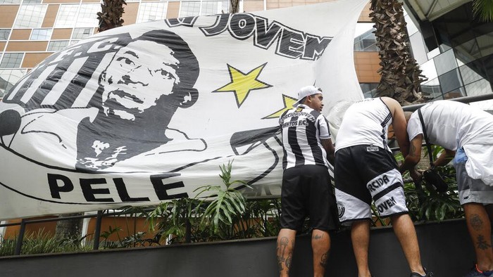 Santos soccer team supporters secure a banner with the image of former soccer star Pele, in front of the Albert Einstein hospital where he is hospitalized in Sao Paulo, Brazil, Sunday, Nov. 4, 2022. The 82-year-old Pele has been at the hospital since Tuesday and officials say he is responding well to treatment for a respiratory infection. (AP Photo/Marcelo Chello)