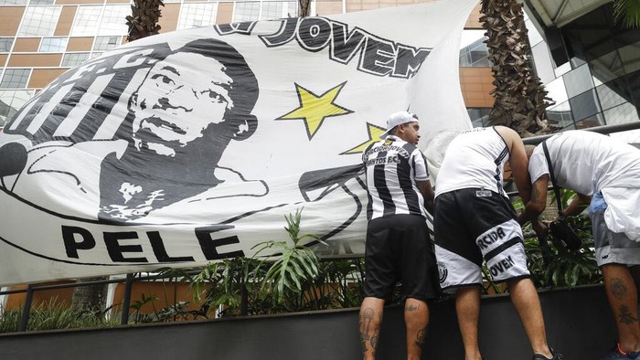 Doakan Kesembuhan Pele, Ratusan Pendukung Berkumpul di RS Santos soccer team supporters secure a banner with the image of former soccer star Pele, in front of the Albert Einstein hospital where he is hospitalized in Sao Paulo, Brazil, Sunday, Nov. 4, 2022. The 82-year-old Pele has been at the hospital since Tuesday and officials say he is responding well to treatment for a respiratory infection. (AP Photo/Marcelo Chello)
