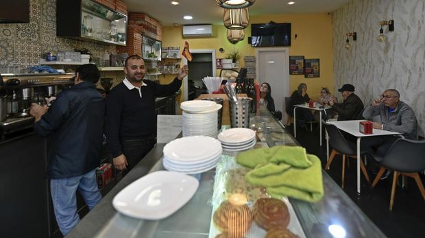 A bar worker waves a small Spanish flag in Spain's north African enclave of Ceuta, Monday, Dec. 5, 2022. The World Cup knockout game between Spain and Morocco on Tuesday will bring millions of fans on both sides of the Strait of Gibraltar together around screens in bars and living rooms to see which country will keep alive its dream of soccer glory. But loyalties be blurred in Spain's north African enclave of Ceuta where identities often mix in unpredictable ways. (AP Photo/Antonio Sempere)