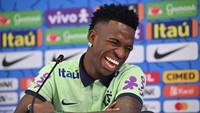 Vinicius Junior tertawa geli melihat ada kucing tiba-tiba menaiki meja konferensi pers Timnas Brasil. (Foto: AFP via Getty Images/NELSON ALMEIDA)