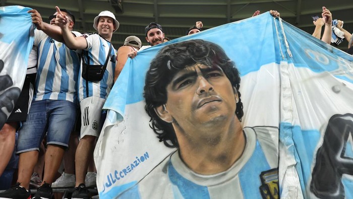 Diego Maradona DOHA, QATAR - DECEMBER 03: Argentina fans hold up a banner bearing a portrait of Diego Armando Maradona as they celebrate the 2-1 victory and passage to the next round following the final whistle of the FIFA World Cup Qatar 2022 Round of 16 match between Argentina and Australia at Ahmad Bin Ali Stadium on December 03, 2022 in Doha, Qatar. (Photo by Youssef Loulidi/Fantasista/Getty Images)