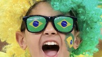 Seorang anak memakai kacamata dan rambut palsu berwarna kuning hijau untuk mendukung Timnas Brasil. (Mohammed Dabbous/Getty Images)