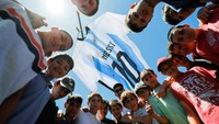 Anak-anak dengan sukacita berfoto di bawah jersey raksasa Messi. 
