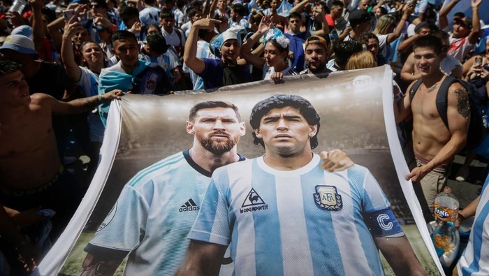 TOPSHOT - Fans of Argentina hold a flag depicting Argentine football stars Lionel Messi (L) and late Diego Maradona (R) while gathering at the Obelisk to celebrate winning the Qatar 2022 World Cup against France in Buenos Aires, on December 18, 2022. (Photo by Emiliano Lasalvia / AFP) (Photo by EMILIANO LASALVIA/AFP via Getty Images)