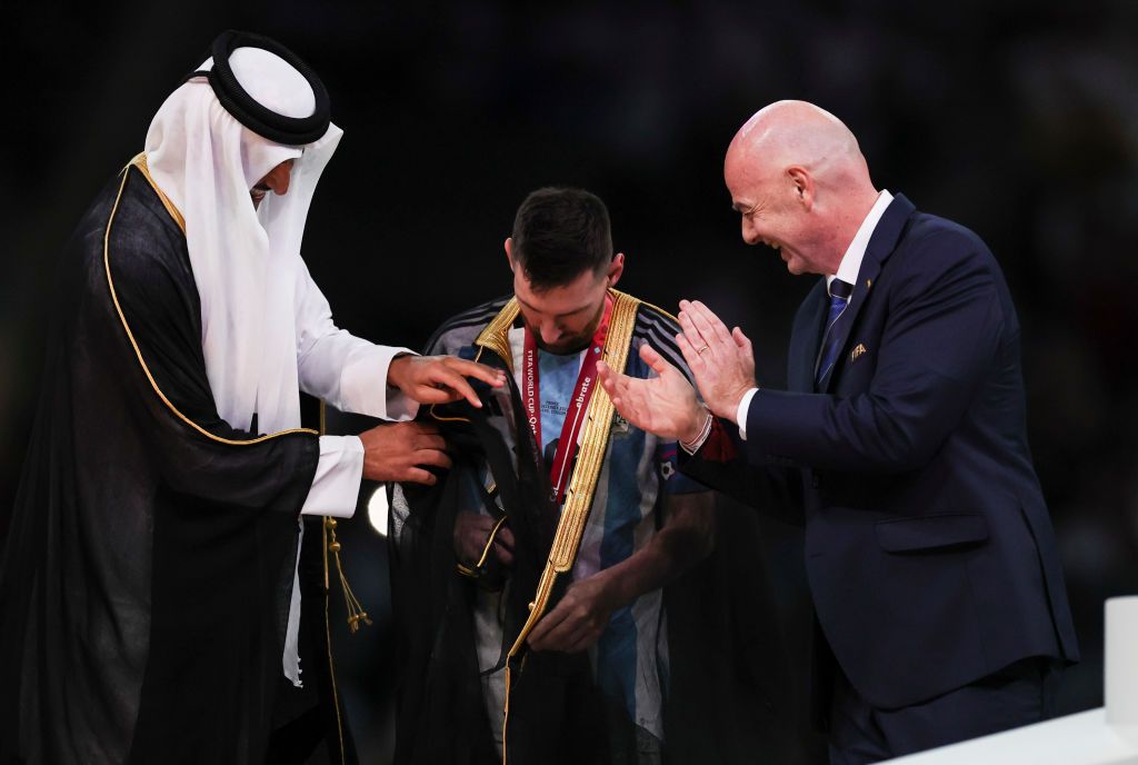 LUSAIL CITY, QATAR - DECEMBER 18:  Lionel Messi of Argentina is presented a traditional black bisht robe by Sheikh Tamim bin Hamad Al Thani, Emir of Qatar, while Gianni Infantino, President of FIFA, looks on after the FIFA World Cup Qatar 2022 Final match between Argentina and France at Lusail Stadium on December 18, 2022 in Lusail City, Qatar. (Photo by Ian MacNicol/Getty Images)
