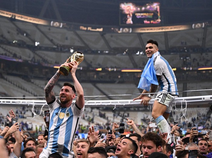 Argentina's forward #10 Lionel Messi (C) lifts the FIFA World Cup Trophy as he celebrates with Argentina's forward #22 Lautaro Martinez and supporters winning the Qatar 2022 World Cup final football match between Argentina and France at Lusail Stadium in Lusail, north of Doha on December 18, 2022. (Photo by Kirill KUDRYAVTSEV / AFP) (Photo by KIRILL KUDRYAVTSEV/AFP via Getty Images)