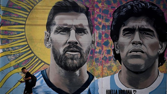 TOPSHOT - A man passes by a mural depicting Argentine football stars Lionel Messi (L) and late Diego Maradona (R) in the eve of Qatar 2022 World Cup final football match between Argentina and France in Buenos Aires, on December 16, 2022. (Photo by Luis ROBAYO / AFP) (Photo by LUIS ROBAYO/AFP via Getty Images)