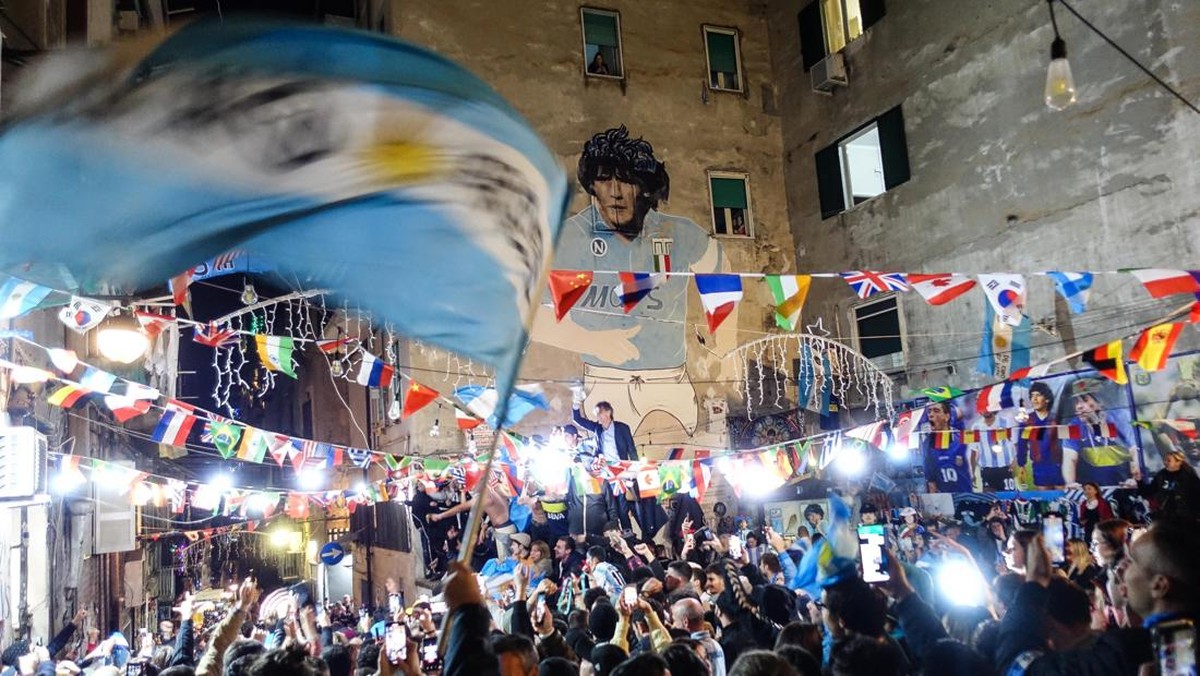 Fans Napoli membentangkan bendera Argentina di depan mural Maradona. (Foto: ANSA/AFP via Getty Images/CESARE ABBATE)