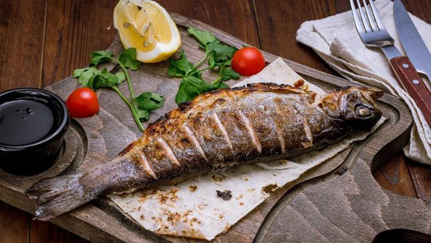 grilled trout on grill on a wooden board with lemon on wooden table