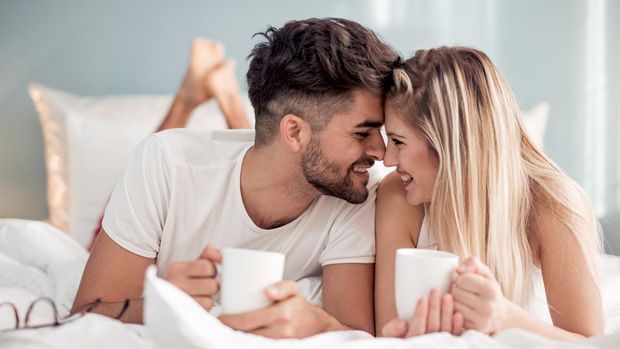 Young beautiful couple drinking coffee in bed at morning.
