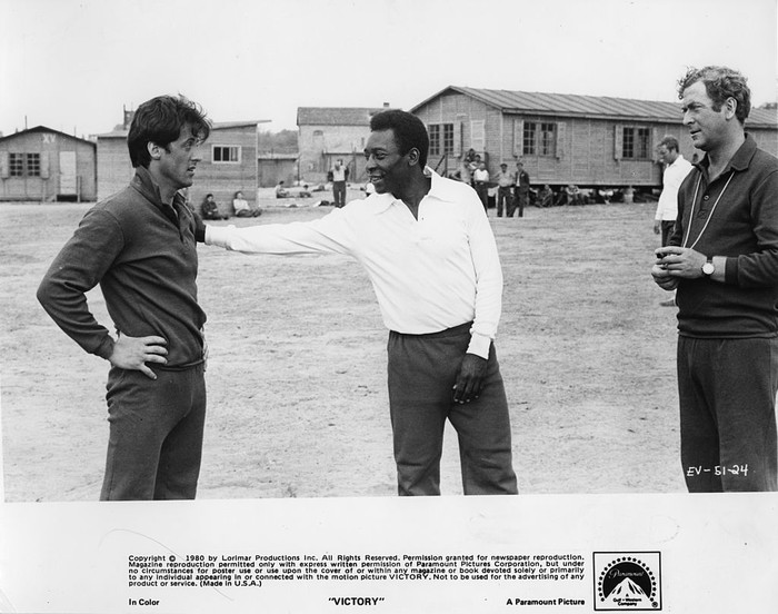 Pele, Stallone CIRCA 1980: Sylvester Stallone is patted by Pele as Michael Caine looks on in a scene for the Paramount Pictures movie