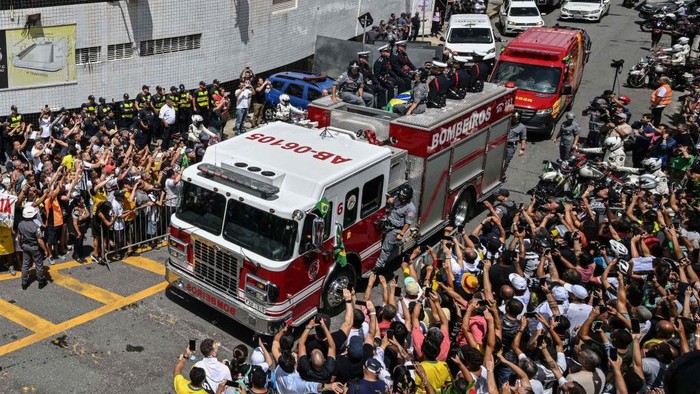 Fans of the late Brazilian football star Pele gather outside the Urbano Caldeira stadium as a firetruck transports Pele's coffin to the Santos' Memorial Cemetery in Santos, Sao Paulo state, Brazil on January 3, 2023. - The funeral procession through Santos will go past the house of Pele's mother, 100-year-old Celeste Arantes, who is still alive. It will end at Santos's Memorial Cemetery, where a Catholic funeral service will be held before Pele is interred in a special mausoleum. (Photo by NELSON ALMEIDA / AFP) (Photo by NELSON ALMEIDA/AFP via Getty Images)