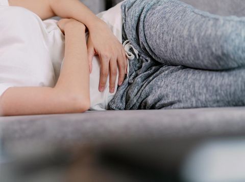 Asian woman having pain on her stomachache or Pelvic pain. housewife hands squeezing on the stomach while sitting on a sofa in the living room at home as suffering from menstruation cramp.