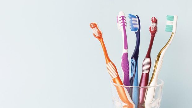 Multi-colored toothbrushes in a glass cup, blue background