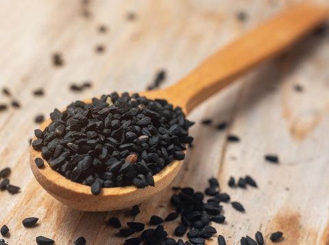 Black cumin seeds on wooden spoon on wooden background.