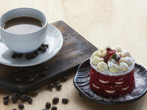 Hot coffee in a white cup and coffee beans on the wooden table. Delicious cake with strawberry on top.
