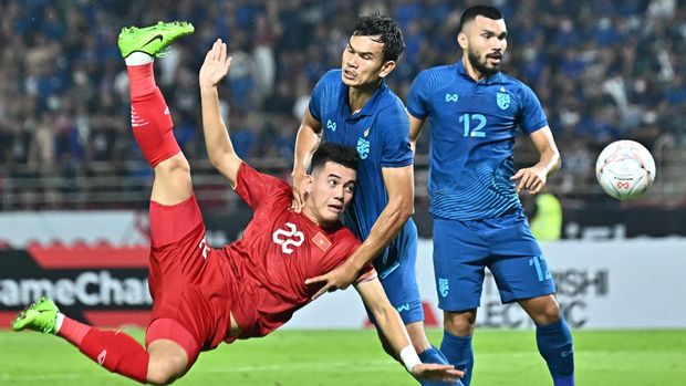 Vietnam's Nguyen Tien Linh (L) jumps in the air after a shot as Thailand's Adisak Kraisorn and Thailand's Kritsada Kaman (R) look on during the second leg of the AFF Cup final football match between Vietnam and Thailand at Thammasat Stadium in Bangkok on January 16, 2023. (Photo by Lillian SUWANRUMPHA / AFP)