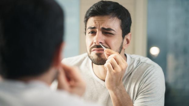 Young hispanic people and male beauty. Metrosexual man feeling pain when trimming nose hair with tweezers