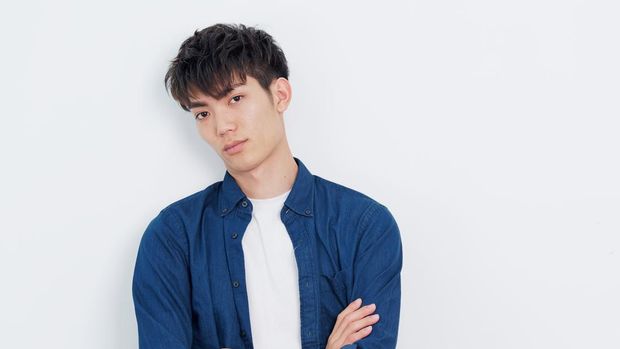 Portrait of a handsome Chinese young man in blue shirt looking at camera with two arms crossed, serious expression, isolated on white background.