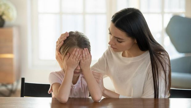 Caring mother calming and hugging crying upset little daughter, sitting at desk together, loving mum expressing support, comforting offended preschool girl, children psychologist concept