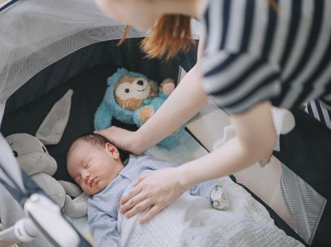 asian chinese young mother putting her infant baby boy in crib in bedroom