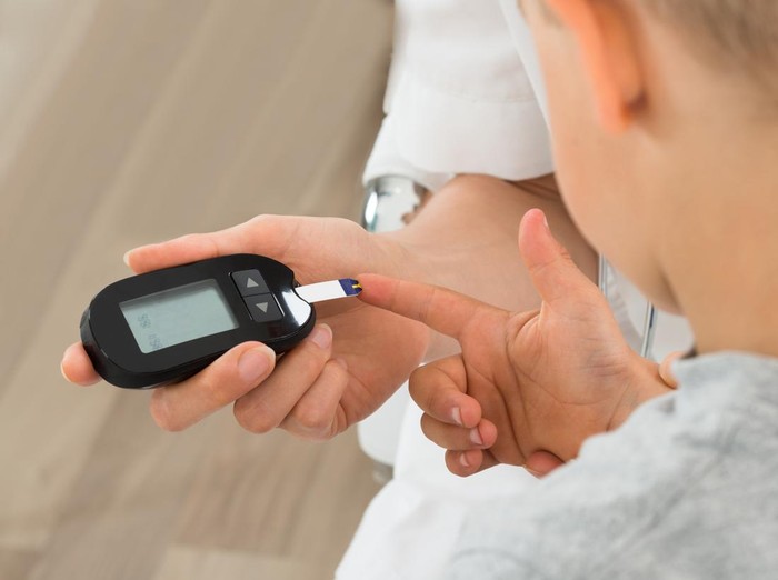 Ilustrasi Diabetes pada Anak Close-up Of Doctor Measuring Blood Sugar Of Child Patient With Glucometer