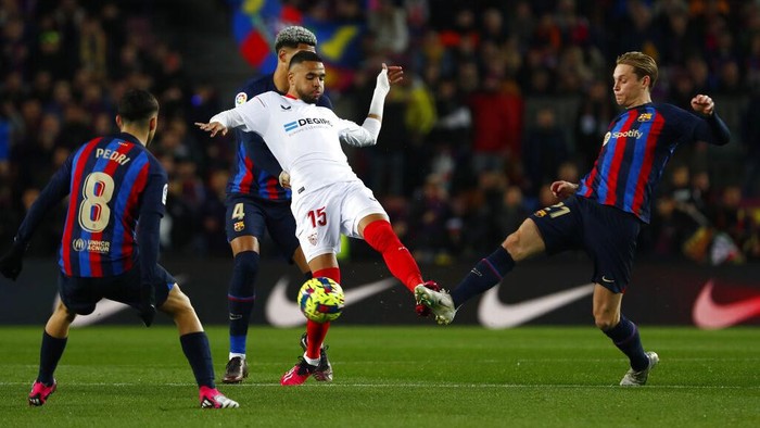 Barcelona Menjauh dari Kejaran Real Madrid Usai Membungkam Sevilla Sevilla's Youssef En-Nesyri, center, challenges for the ball with Barcelona's Frenkie de Jong, right, and Barcelona's Pedri, left, and Barcelona's Ronald Araujo during a Spanish La Liga soccer match between Barcelona and Sevilla at the Camp Nou stadium in Barcelona, Spain, Sunday, Feb. 5, 2023. (AP Photo/Joan Monfort)