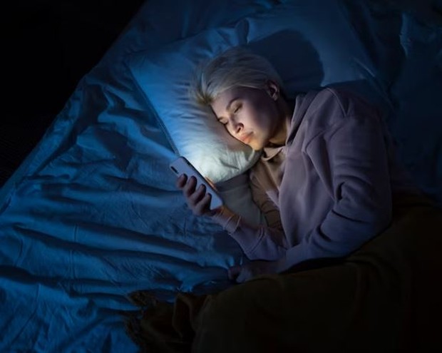 Perempuan menatap layar handphone sebelum tidur