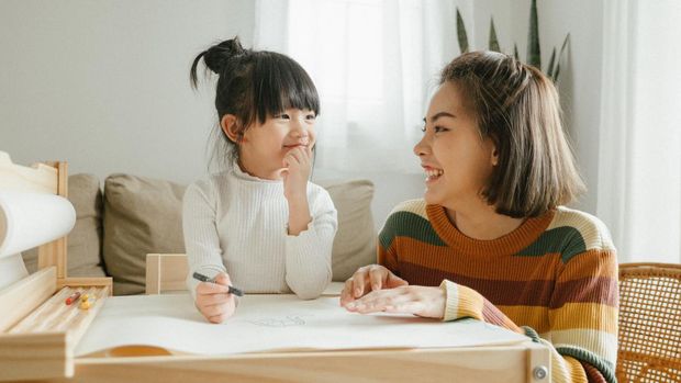 Cute and lovely asian little girl doing homework at home, with a help of her mother.