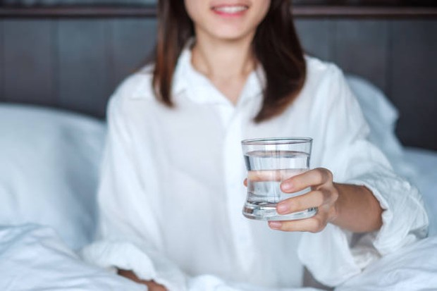 Gambaran perempuan muda yang memegang segelas air putih.